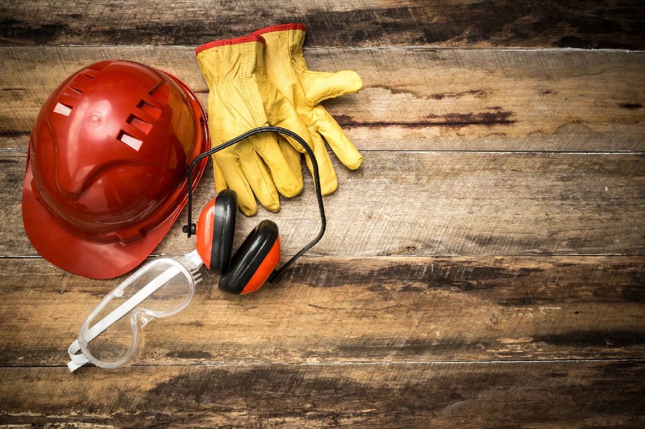 A hard hat, ear muffs and gloves on top of a wooden table.