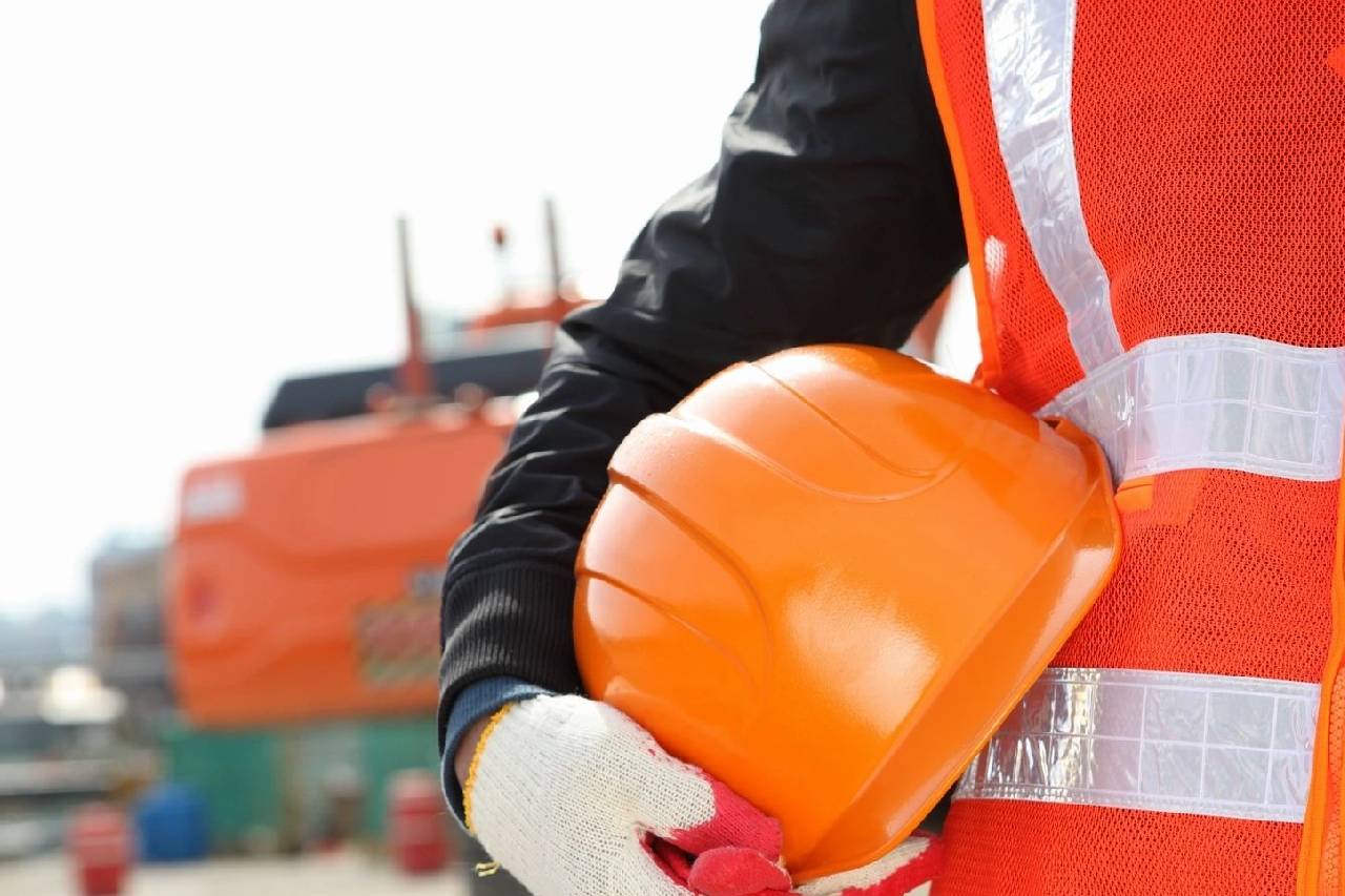 A construction worker holding an orange helmet.